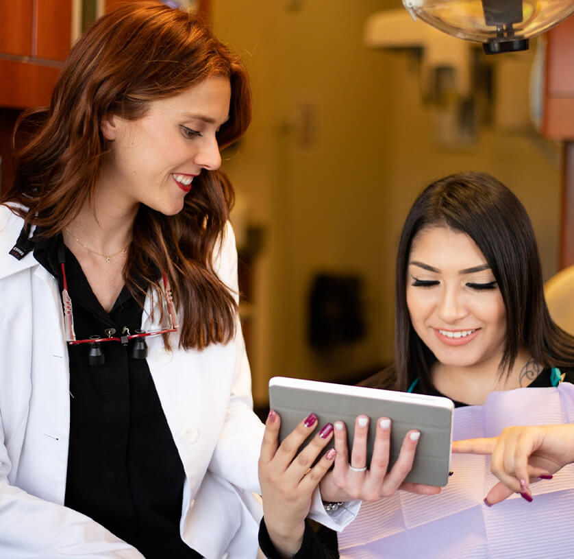 female red haired dentist showing a tablet to a smiling female patient